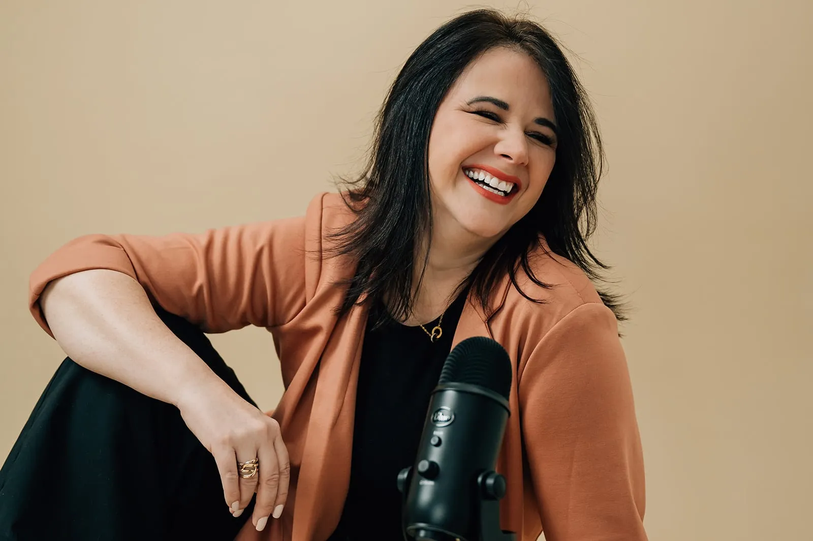 Luísa Marteleto smiling, wearing a terracotta blazer and holding a microphone