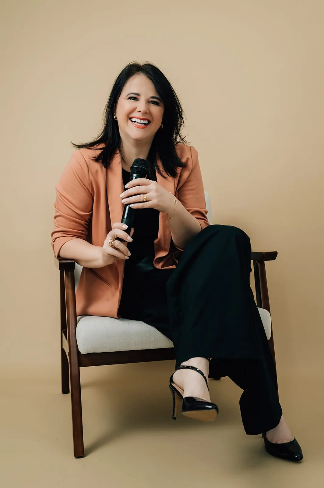 Luísa Marteleto sitting in an armchair, smiling, holding a microphone